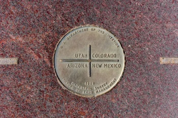 Placa redonda de bronce del Monumento de Cuatro Esquinas incrustada en granito rojo, mostrando los nombres de Utah, Colorado, Arizona y Nuevo México