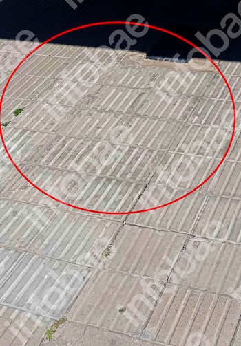 Vista cenital de un pavimento de baldosas grises rectangulares con un hueco oscuro y pequeño en la parte superior. Un círculo rojo resalta la zona del hueco