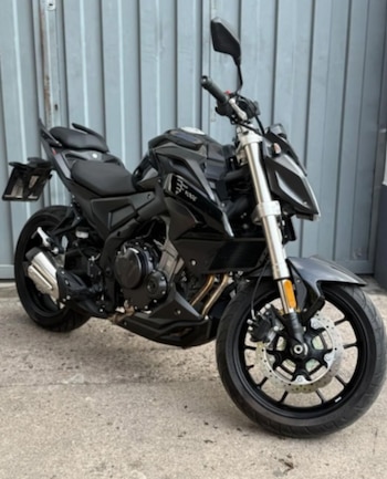 Una motocicleta de color negro marca Voge permanece estacionada frente a un portón metálico gris