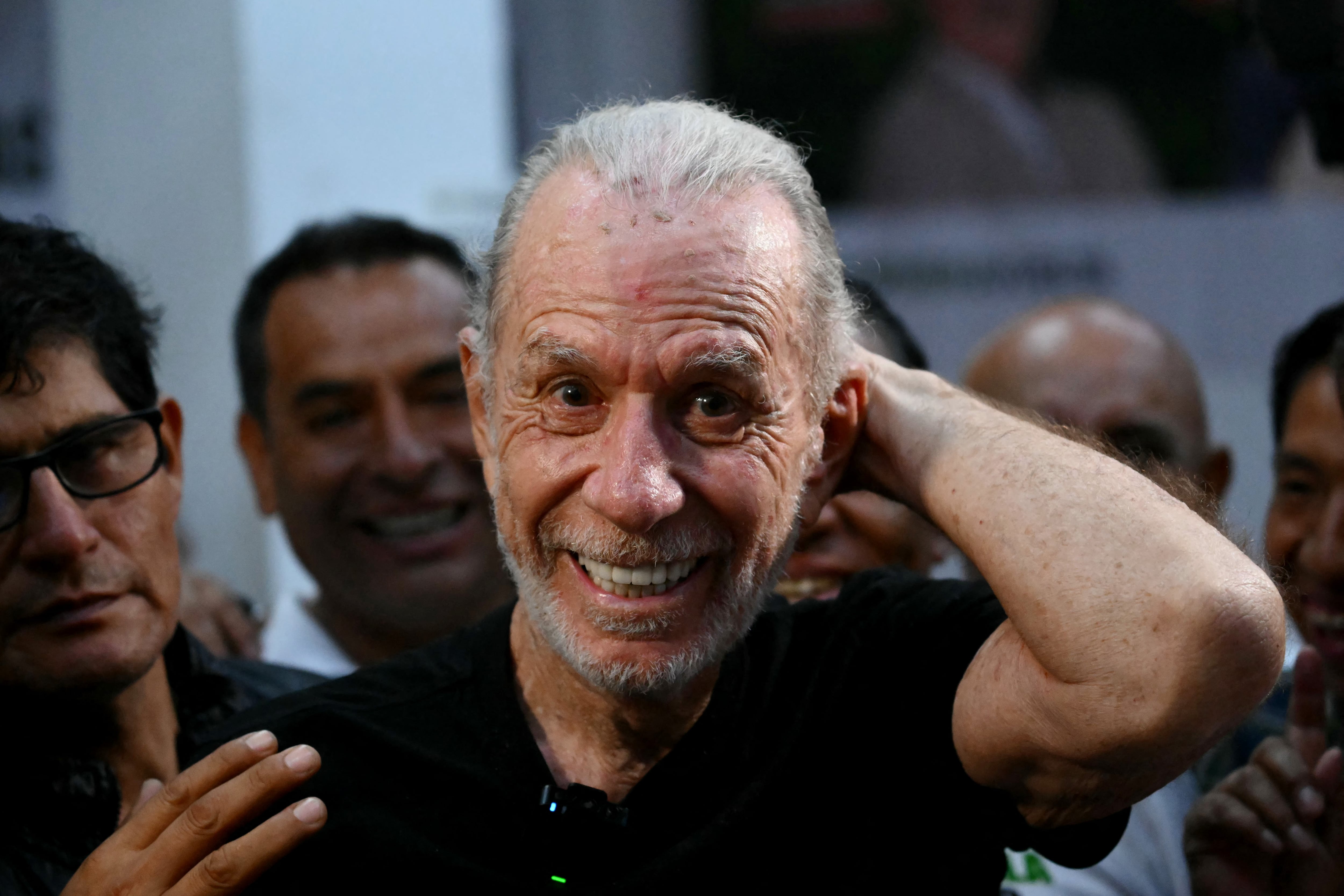 Ricardo Belmont, conocido político y candidato presidencial, participa en un acto de campaña de cara a las Elecciones Perú, donde se le ve sonriendo y tocándose la cabeza en medio de una multitud.