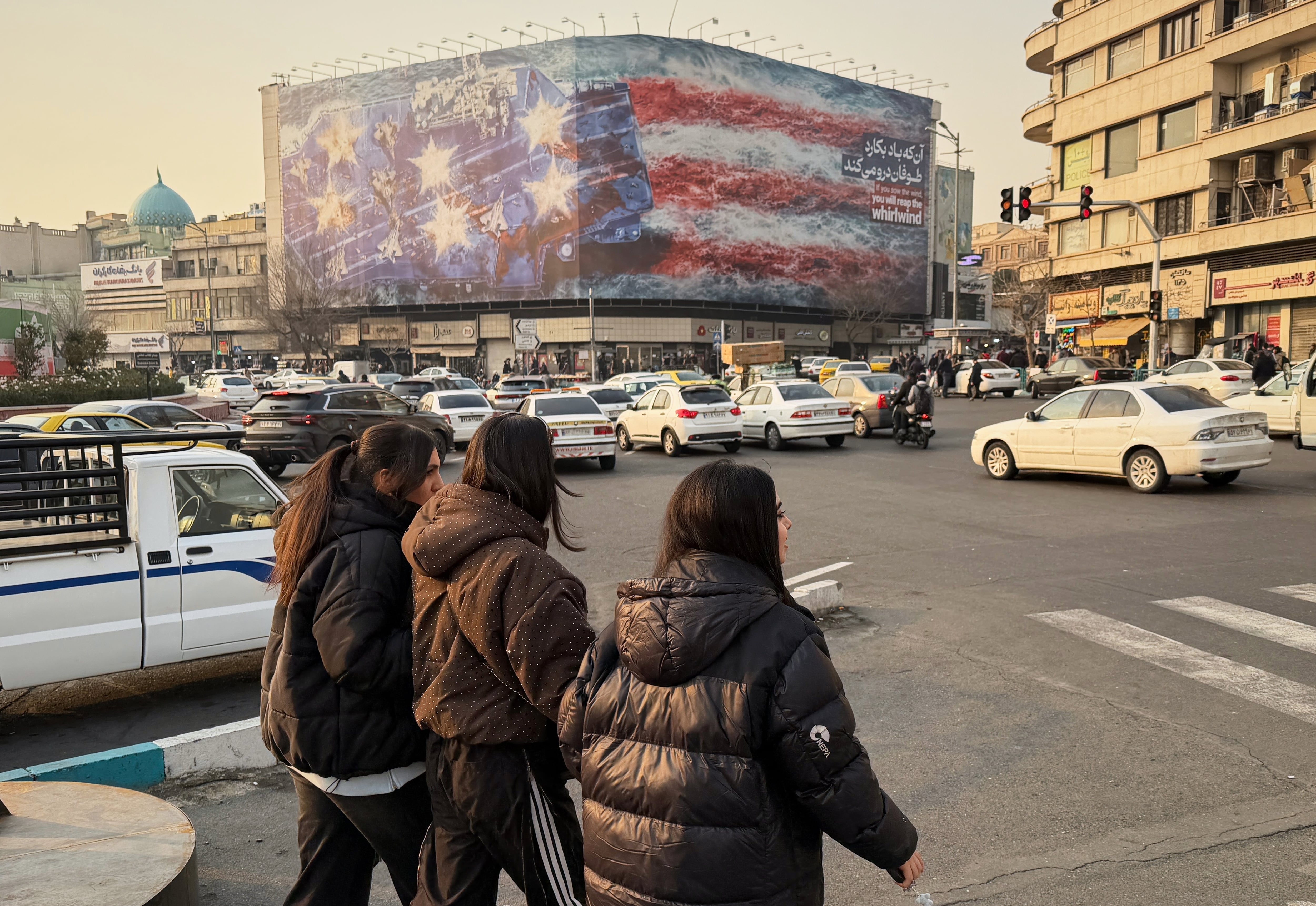 Personas caminan frente a un cartel que muestra un portaaviones estadounidense destruido en Teherán. Las autoridades iraníes se muestran desafiantes ante las amenazas de Trump. (AP Foto/Vahid Salemi)