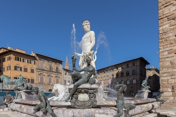 Vista frontal de la Fontana del Nettuno en la Piazza della Signoria, con la gran estatua de mármol blanco de Neptuno y figuras acuáticas de bronce, bajo un cielo azul