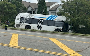 Un autobús blanco del transporte público MARTA inclinado sobre la hierba junto a varios árboles cerca de una carretera asfaltada