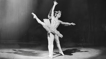 Fotografía en blanco y negro de una bailarina con tutú y tiara junto a un bailarín sobre un escenario iluminado