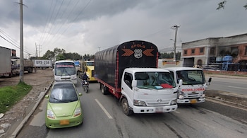 Carretera asfaltada con flechas pintadas en el suelo, un letrero verde con indicaciones hacia Bogotá y Funza, vehículos y árboles