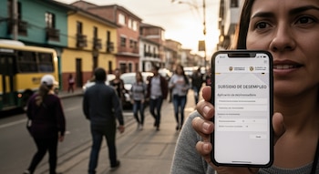 Primer plano de una mujer sosteniendo un smartphone que muestra una aplicación de "SUBSIDIO DE DESEMPLEO", con una calle urbana borrosa detrás.