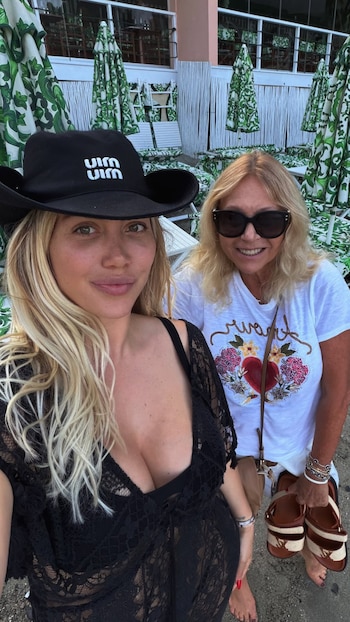 Selfie de dos mujeres. Una con sombrero negro y vestido de encaje. La otra con gafas de sol, camiseta blanca, y sandalias. Sombrillas