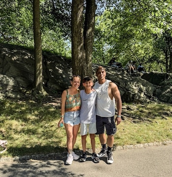 Un niño posa junto a una mujer y un hombre en un parque con vegetación y rocas de fondo