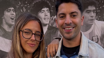 Nati Jota y Gastón Edul posan sonrientes frente a un mural blanco y negro con varias imágenes de Diego Maradona, incluyendo una camiseta de AFA.