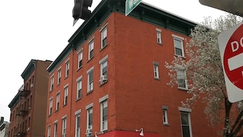 Edificio de ladrillo rojo de varias plantas con muchas ventanas y aires acondicionados, y un árbol con flores blancas en una esquina de Hoboken