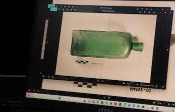 Una pantalla de computadora portátil exhibe una imagen de una botella de vidrio verde fracturada y una escala de centímetros en un fondo blanco