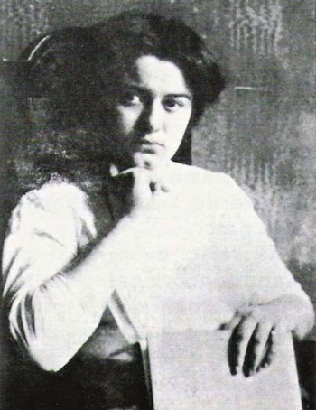 Fotografía en blanco y negro de una mujer joven con cabello oscuro que apoya la mano en la barbilla y sostiene un papel
