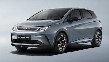 Un BYD Dolphin Comfort gris oscuro de cuatro puertas, visto desde un ángulo frontal izquierdo, sobre un fondo liso de color gris claro