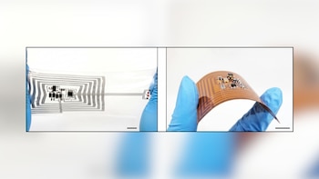Manos con guantes azules sostienen dos circuitos electrónicos flexibles, uno transparente con trazados grises y otro de color café doblado