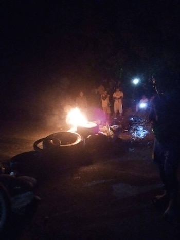 Imagen nocturna de varias personas alrededor de una fogata hecha con neumáticos encendidos, que ilumina un área oscura