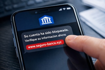 Primer plano de un smartphone que muestra un SMS de phishing con un logo bancario azul y un enlace fraudulento en rojo. Un dedo se acerca al enlace.
