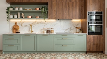 Una cocina moderna con gabinetes inferiores verdes, superiores de madera, una encimera y salpicadero de mármol blanco, electrodomésticos de acero, y piso de baldosas con patrón.