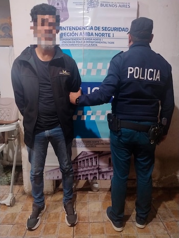 Un oficial de policía uniformado, de espaldas, sujeta a un hombre con rostro pixelado. Al fondo, un cartel con texto del Gobierno de Buenos Aires