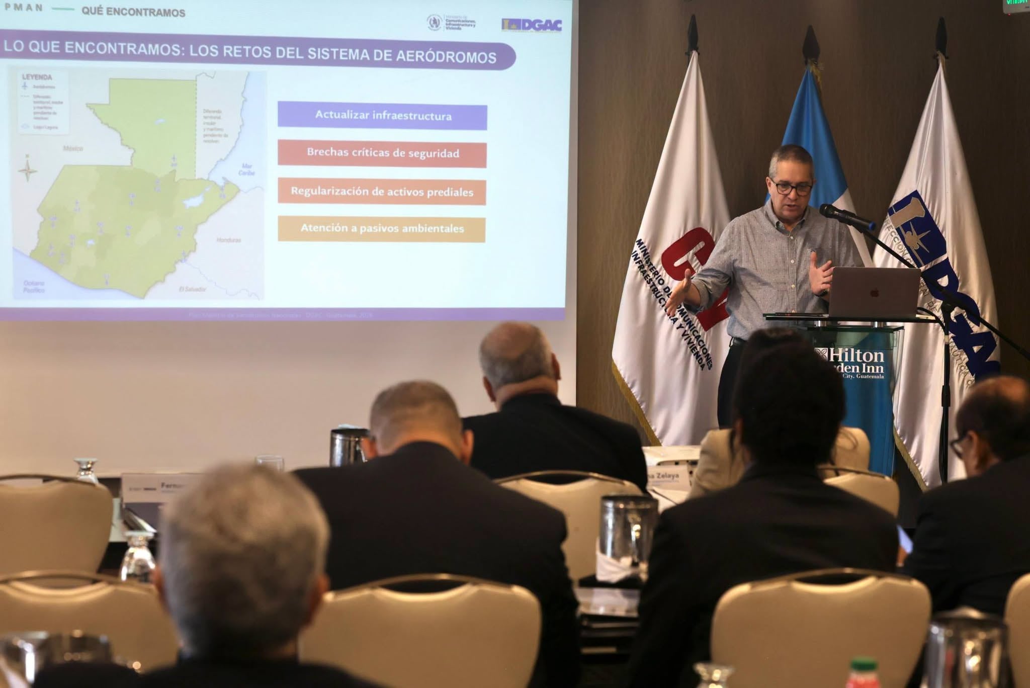 Un ponente expone los retos del sistema de aeródromos frente a una pantalla del Ministerio de Comunicaciones, Infraestructura y Vivienda en Guatemala. (DGAC)