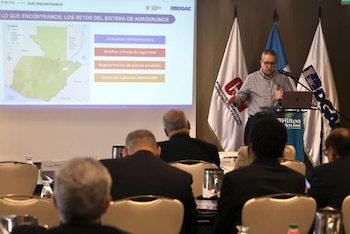 Un hombre expone desde un podio junto a una proyección con el mapa de Guatemala y texto, frente a varias personas sentadas de espaldas