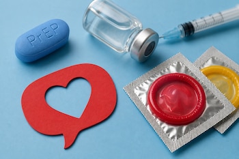 Una píldora azul con la sigla PrEP, un frasco de vidrio, una jeringa, dos preservativos en empaque y una figura de papel rojo con un corazón.