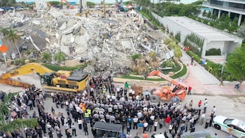 Gran pila de escombros del condominio Champlain Towers South en Surfside, Florida, con excavadora, grúa y una multitud de personas, incluyendo equipos de rescate, en la base
