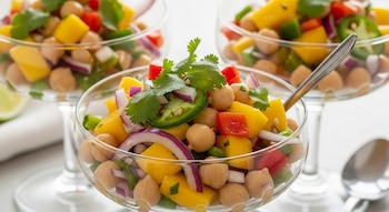 Primer plano de tres copas de vidrio con ceviche de garbanzo y mango, cebolla morada, pimiento rojo, rodaja de jalapeño y cilantro fresco.