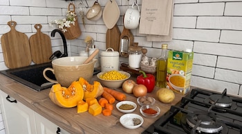 Calabaza, zanahorias, granos de choclo, cebollas, morrón, papa, aceite, caldo de verduras, comino, nuez moscada, páprika, sal y pimienta sobre una encimera de cocina.