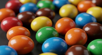 Múltiples chocolates confitados redondos y ovalados de colores rojo, amarillo, verde, naranja, azul y marrón, sobre una superficie oscura.