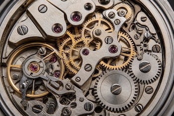 Engranajes dorados y plateados, tornillos de metal y pequeñas piedras de color púrpura en el interior de un reloj mecánico.