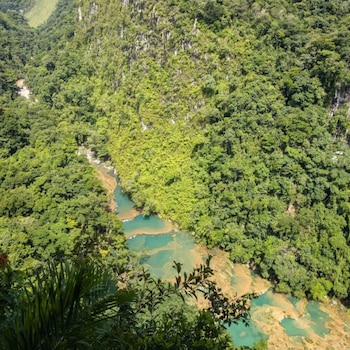 Vista aérea de un denso bosque tropical con un río de agua turquesa que forma piscinas naturales escalonadas en un paisaje montañoso verde y exuberante