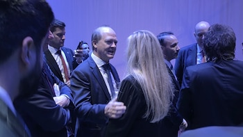 Varias personas con traje formal conversan de pie dentro de un salón iluminado por luces de tono azul