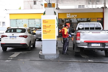 Playero de Shell carga combustible a camioneta plateada en estación de servicio. Se ven surtidor, precios y un Fiat Cronos blanco estacionado