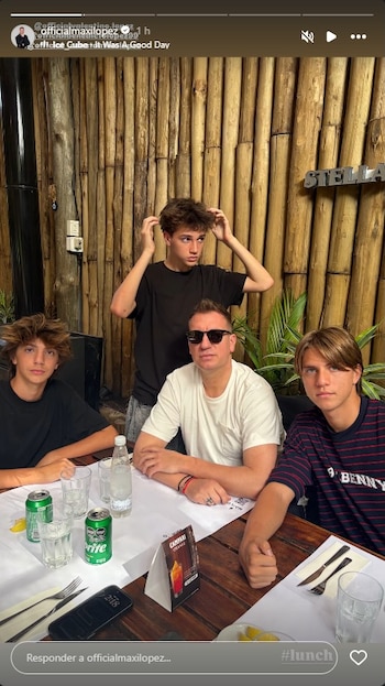 Cuatro hombres sentados alrededor de una mesa de madera con vasos y bebidas, frente a una pared de bambú. Uno de ellos lleva gafas de sol