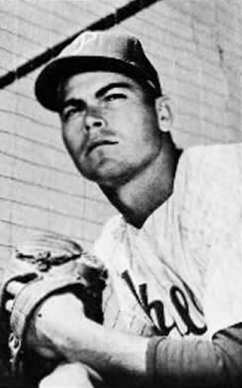 Retrato en blanco y negro de Jack Lohrke, jugador de béisbol, vestido con uniforme y gorra, sosteniendo un guante, con una valla en el fondo