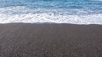 Arena fina de color negro en la orilla del mar con espuma blanca producida por las olas.