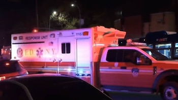Una ambulancia y un camión de bomberos del FDNY con luces de emergencia activas se ven en una calle urbana durante la noche