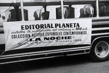 Lateral de un autobús de línea con una pancarta blanca que anuncia el volumen número cien de Editorial Planeta y la obra La Noche de 1959