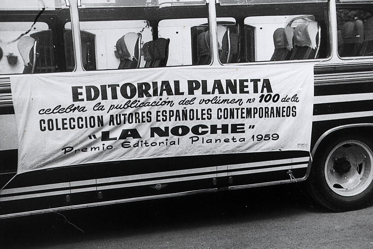 Un autobús lleva colgada una pancarta conmemorativa de Editorial Planeta sobre la publicación del volumen cien de la colección Autores Españoles Contemporáneos y el Premio Planeta 1959.