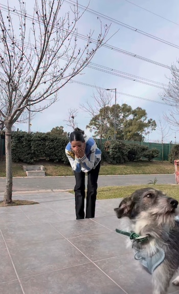 Una mujer inclinada se cubre el rostro con las manos sobre una vereda, junto a un perro pequeño en primer plano