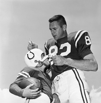 Fotografía en blanco y negro de Raymond Berry, con camiseta de los Colts número 83, mirando a un niño con casco y sujetando un balón de fútbol