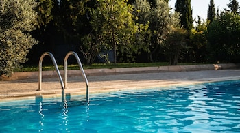 Vista de una piscina con agua azul clara y escaleras metálicas, rodeada por un borde pavimentado y densa vegetación verde, bajo la luz del sol.