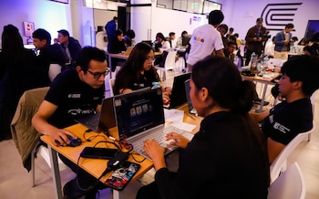 Un grupo de personas sentadas frente a mesas con computadoras portátiles y teléfonos móviles en un salón iluminado