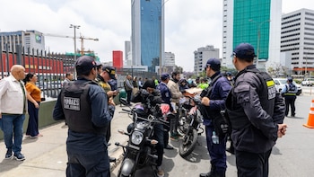 Agentes de seguridad municipal y policías uniformados intervienen a motociclistas en una acera junto a varios edificios