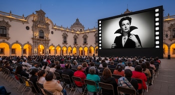 Multitud de personas sentadas en sillas frente a una gran pantalla que muestra el rostro de María Félix. Detrás, un edificio histórico con arcos.