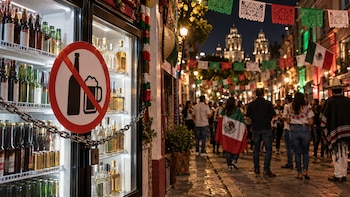 Refrigerador encadenado con botellas y señal de prohibición de alcohol frente a una calle concurrida y decorada por la noche
