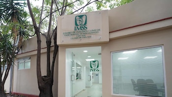 Fachada de un edificio beige con la marquesina del IMSS, una entrada de cristal con puerta abierta y una ventana a la derecha