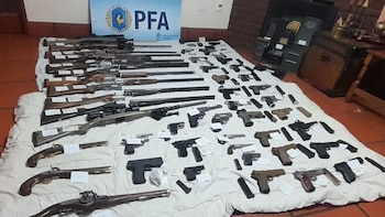 Una gran variedad de armas de fuego, incluyendo numerosos rifles, pistolas de diversos tipos y municiones, se exhiben sobre una tela blanca en el suelo