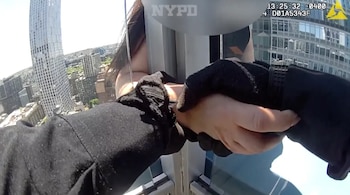 Mano enguantada de un policía sujetando la mano de una mujer en el borde de un rascacielos, con una vista aérea de Brooklyn y otros edificios