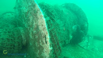 Un tambor de red de pescar cubierto de sedimento en el fondo del mar con agua de tono verdoso